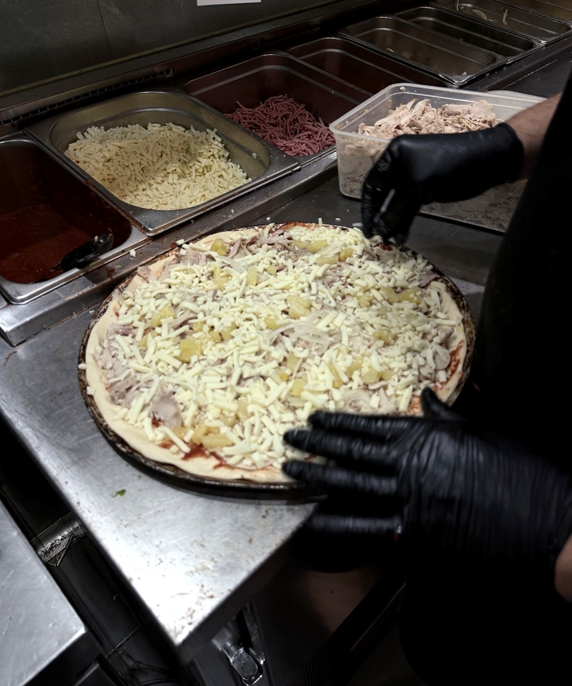 A Newlands Pizza team member preparing a pizza fresh to order